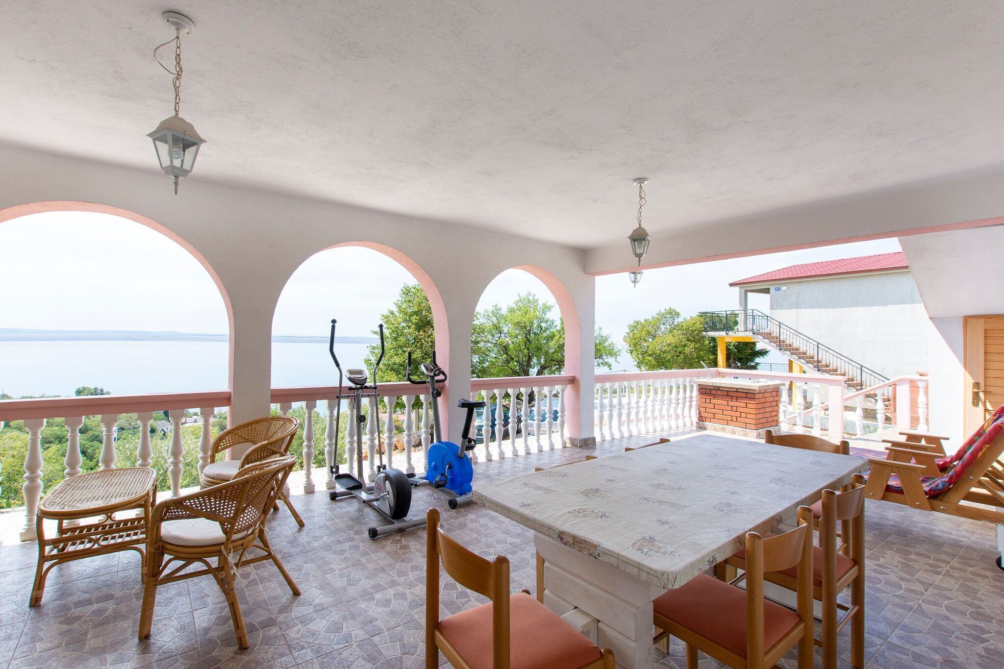 A covered outdoor area with a table and chairs, exercise equipment, and a view of the sea.