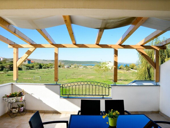 Eine überdachte Terrasse mit Blick auf eine grüne Landschaft und ein Gewässer.