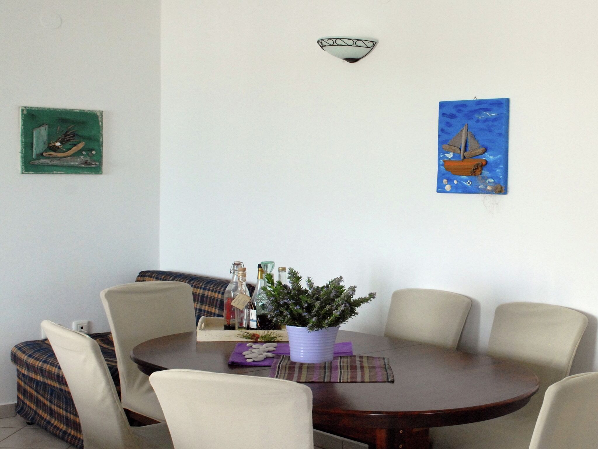 A dining area with a round table, six chairs, a potted plant, and two wall-mounted artworks.