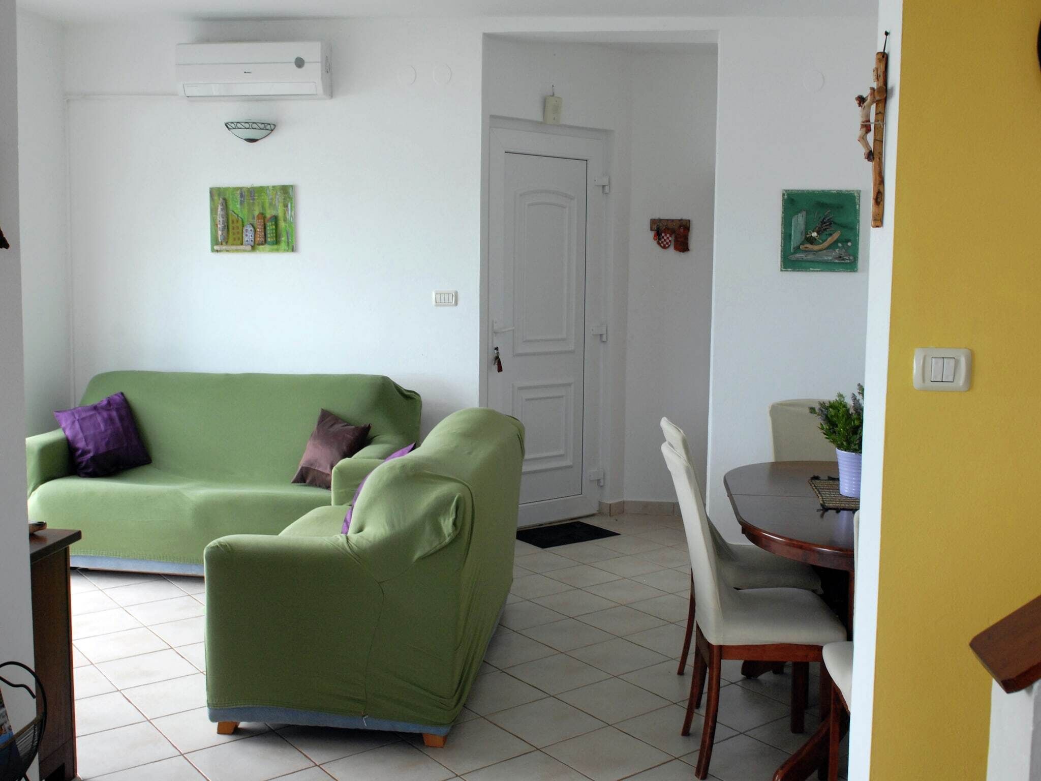 A living room with a green sofa, a dining table with chairs, a white door, and a small table with a plant.