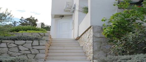 A staircase leading to a white door, flanked by stone walls and greenery.
