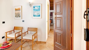Une pièce comprenant deux chaises en bois, une table sur laquelle est disposée une assiette de fruits et deux tableaux encadrés accrochés au mur.