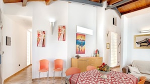 Un coin repas avec une table recouverte d’une nappe à motifs, entourée de chaises orange.