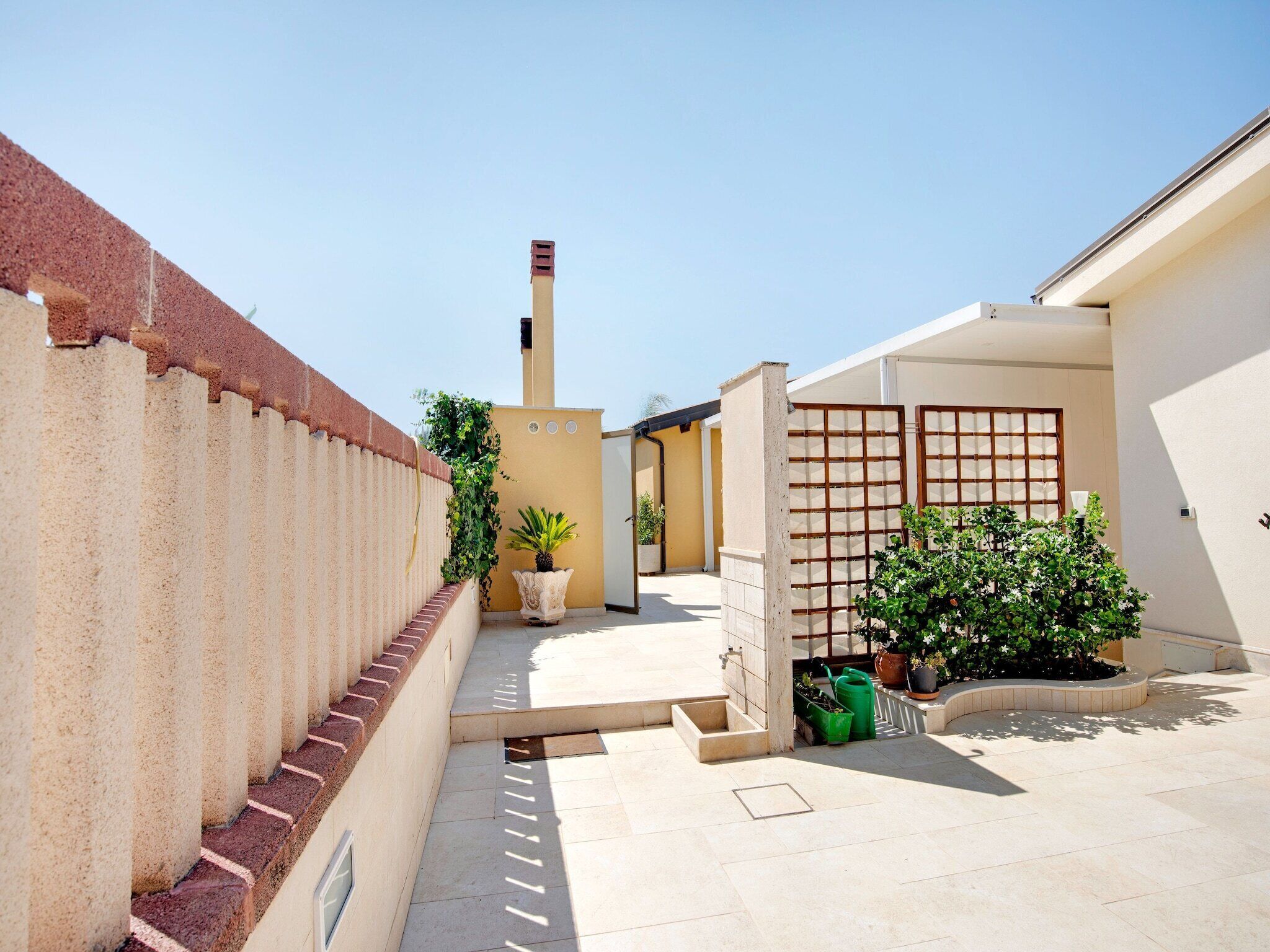 A narrow courtyard with a tiled floor, a brick wall, and a small garden area with potted plants.