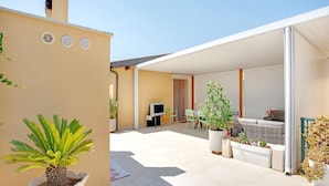 Un patio couvert aménagé avec des sièges, un téléviseur et des plantes en pot.