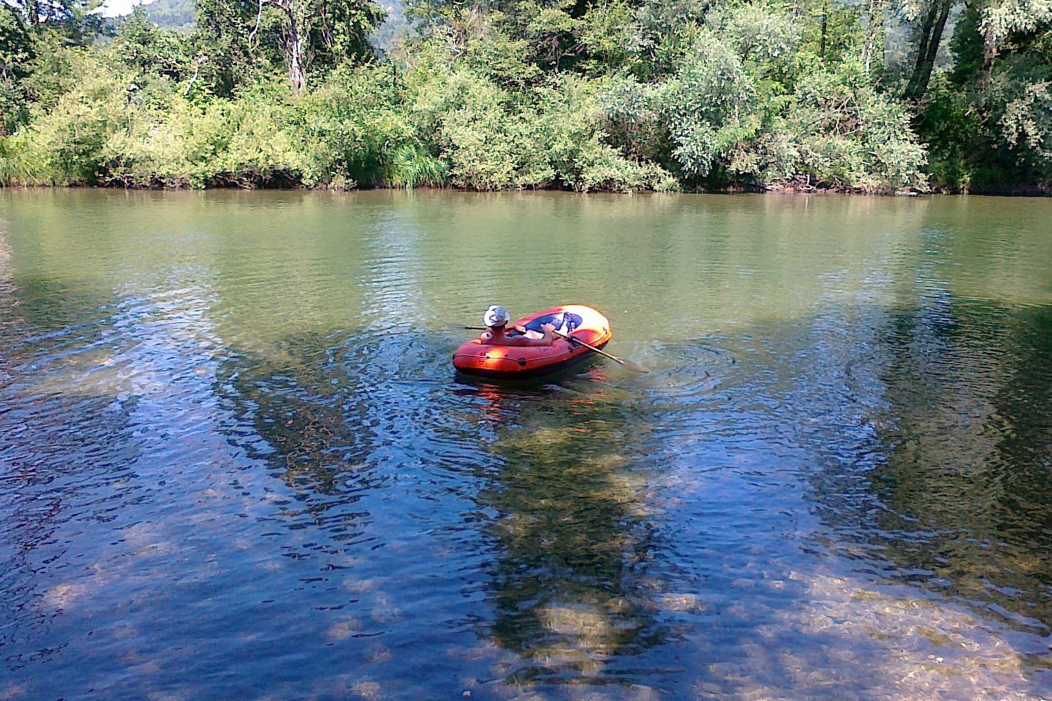 A red inflatable raft on a calm river surrounded by dense greenery.
