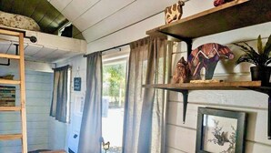 Ein gemütliches Zimmer mit einem Etagenbett, einem kleinen Tisch, einer roten Bank und Regalen mit Dekoration.