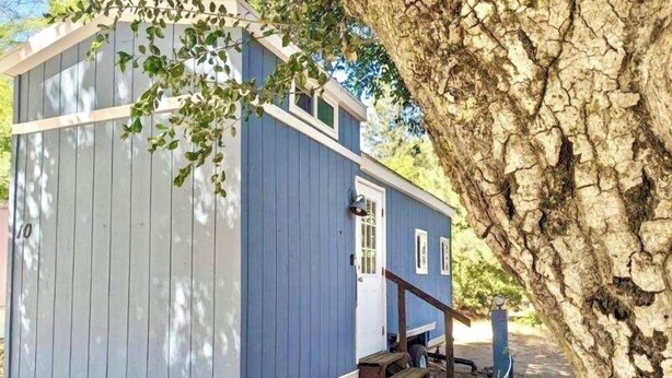 Eine kleine, eingeschossige Holzhütte mit blauer Fassade, einer Haustür und einer kleinen Veranda.