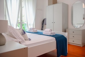 A bedroom with a bed, a wardrobe, a mirror, and a window with curtains.