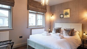 Un lit bien fait, avec des serviettes à disposition, un radiateur, une fenêtre avec des rideaux et un luminaire fixé au mur.