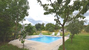 A rectangular swimming pool with a concrete deck, surrounded by a gravel border. There are two white lounge chairs and a small shed in the background. - Holiday Home in Banjole near the Sea (Banjole)