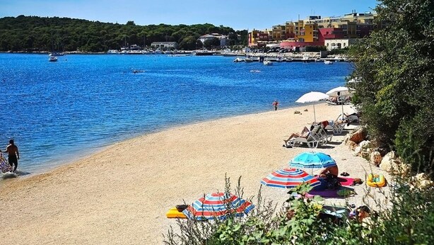 A beach with clear blue water, umbrellas, and a few people. - Holiday Home in Banjole near the Sea (Banjole)