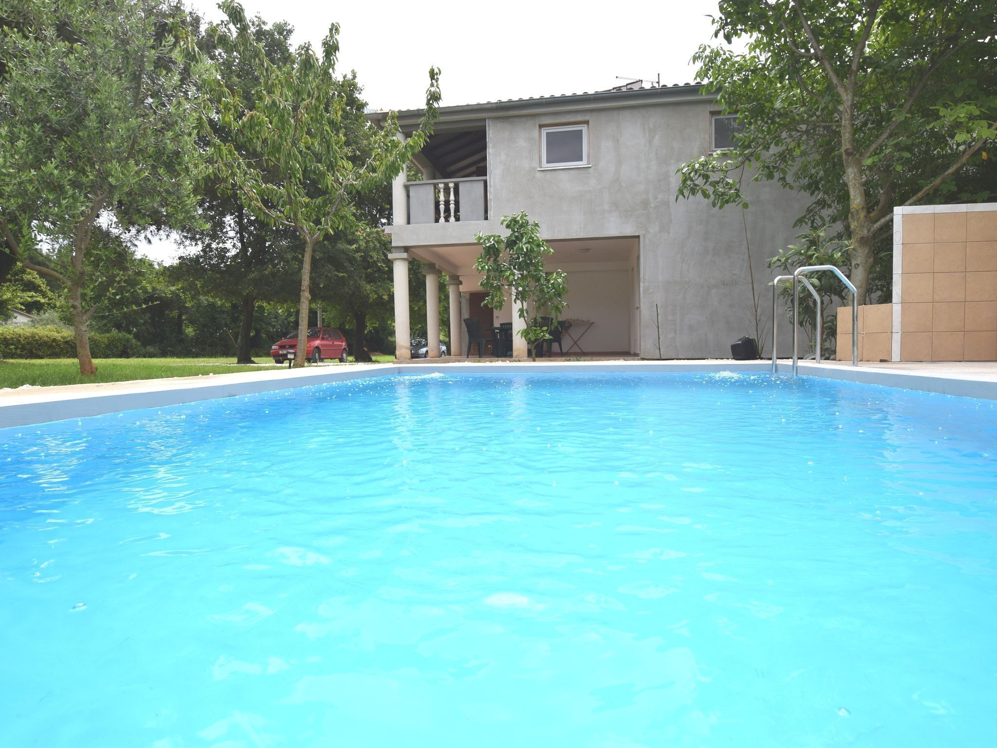 A swimming pool with a covered patio area, a two-story building, and trees in the background.