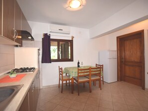 Une cuisine de taille réduite, équipée d’une cuisinière à gaz, d’une table avec des chaises, d’une fenêtre avec des rideaux et d’un réfrigérateur.