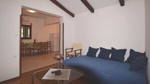 A room with a blue sofa, a small table with a lamp, and a dining area in the background. - Holiday Home in Banjole near the Sea (Banjole)