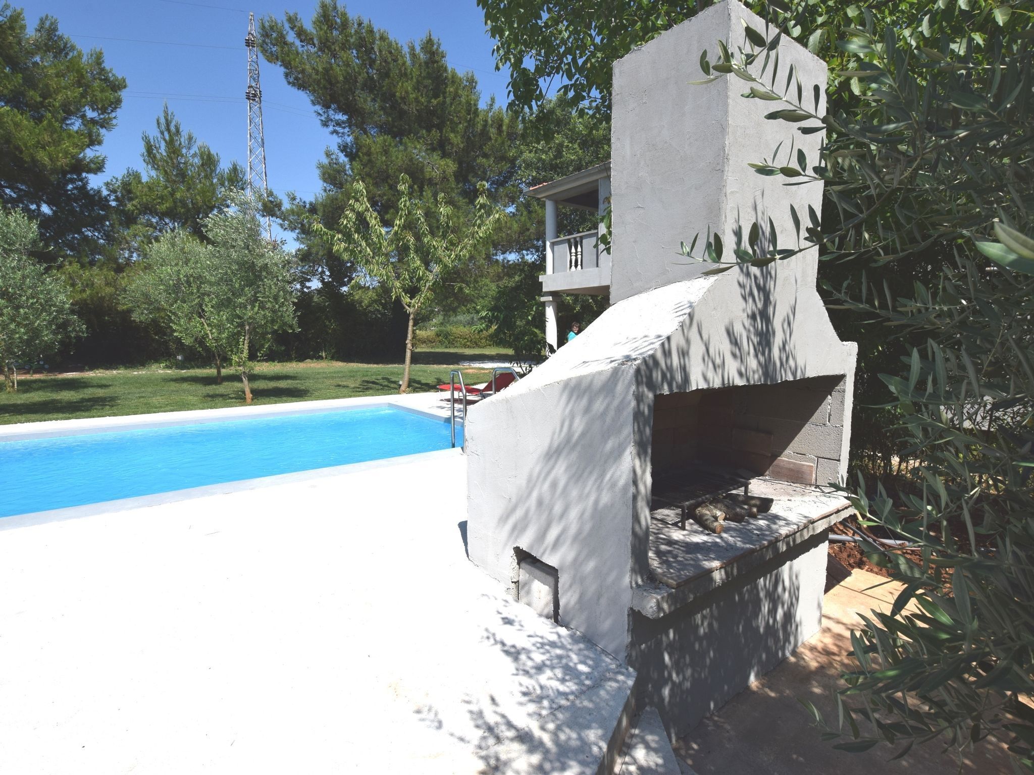 Una piscina con estructura de concreto, rodeada de vegetación y un cielo despejado.