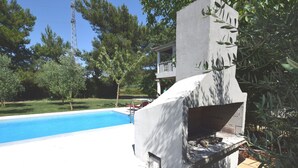 A swimming pool with a concrete structure, surrounded by greenery and a clear sky. - Holiday Home in Banjole near the Sea (Banjole)