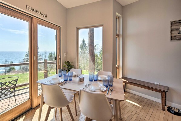 A dining area with a table set for four, large windows offering a view of the sea, and a 'HAPPY PLACE' sign on the wall.