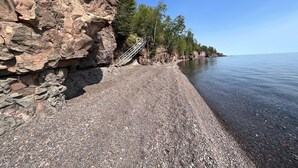 A rocky shoreline with a clear view of the water, a staircase leading up to a cliff, and trees along the edge.