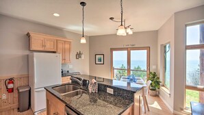 A modern kitchen with granite countertops, wooden cabinets, and a view of the ocean through large windows.