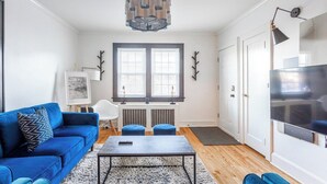 A modern living room with a blue sofa, a coffee table, a large TV, and a unique chandelier. - Wells Whole House (Bridgeport)