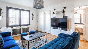 A modern living room with a blue sofa, a coffee table, and a TV mounted on the wall. - Wells Whole House (Bridgeport)