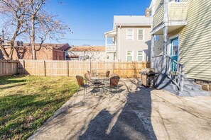 A backyard patio with a table and chairs, a wooden fence, and a house with a blue door. - Wells Whole House (Bridgeport)