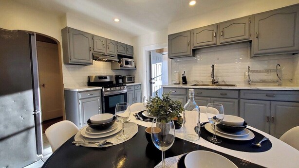 A modern kitchen with grey cabinets, a dining table set for four, and a large window providing natural light. - Wells Whole House (Bridgeport)