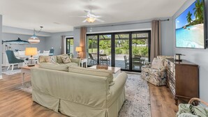 Un salon spacieux avec un grand canapé, un coin repas et une vue sur l’extérieur grâce à de grandes portes-fenêtres coulissantes.