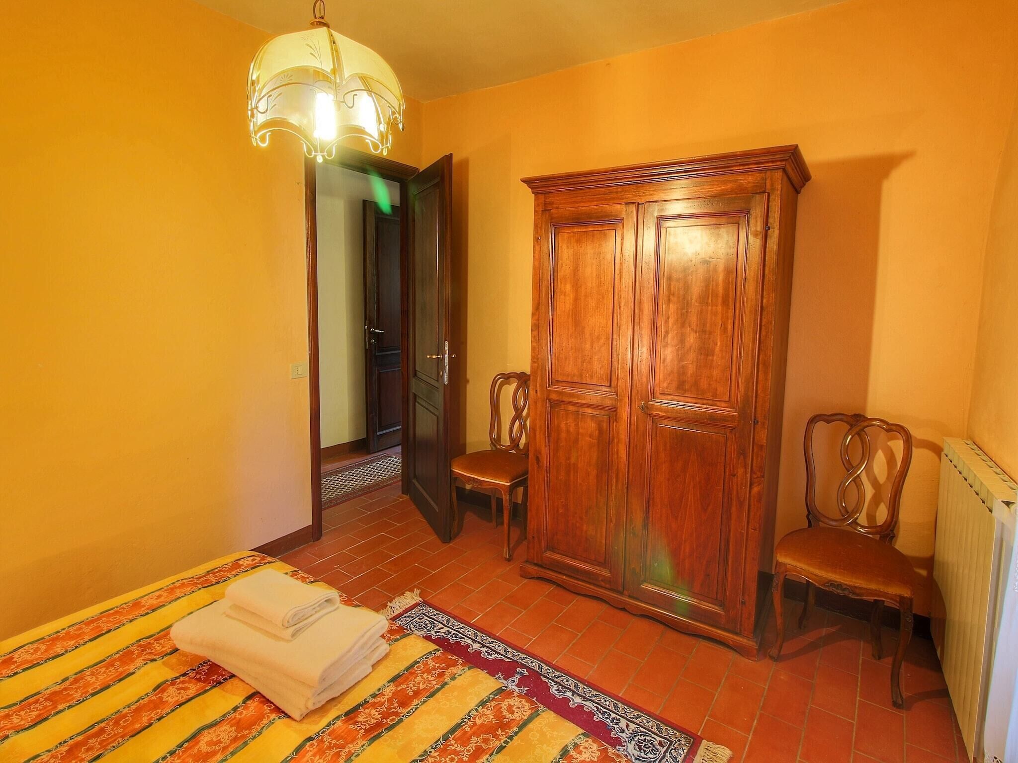 Una habitación con un armario de madera, dos sillas, una cama con colcha a rayas y una araña.