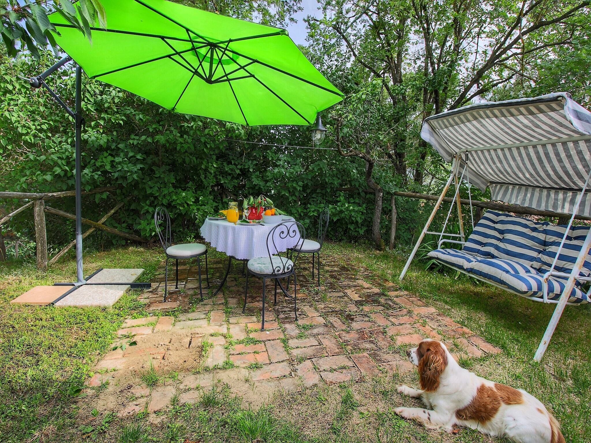 Eine Terrasse mit Esstisch, einer Schaukelstuhlsitzgelegenheit und einem Hund, der auf dem Boden sitzt.