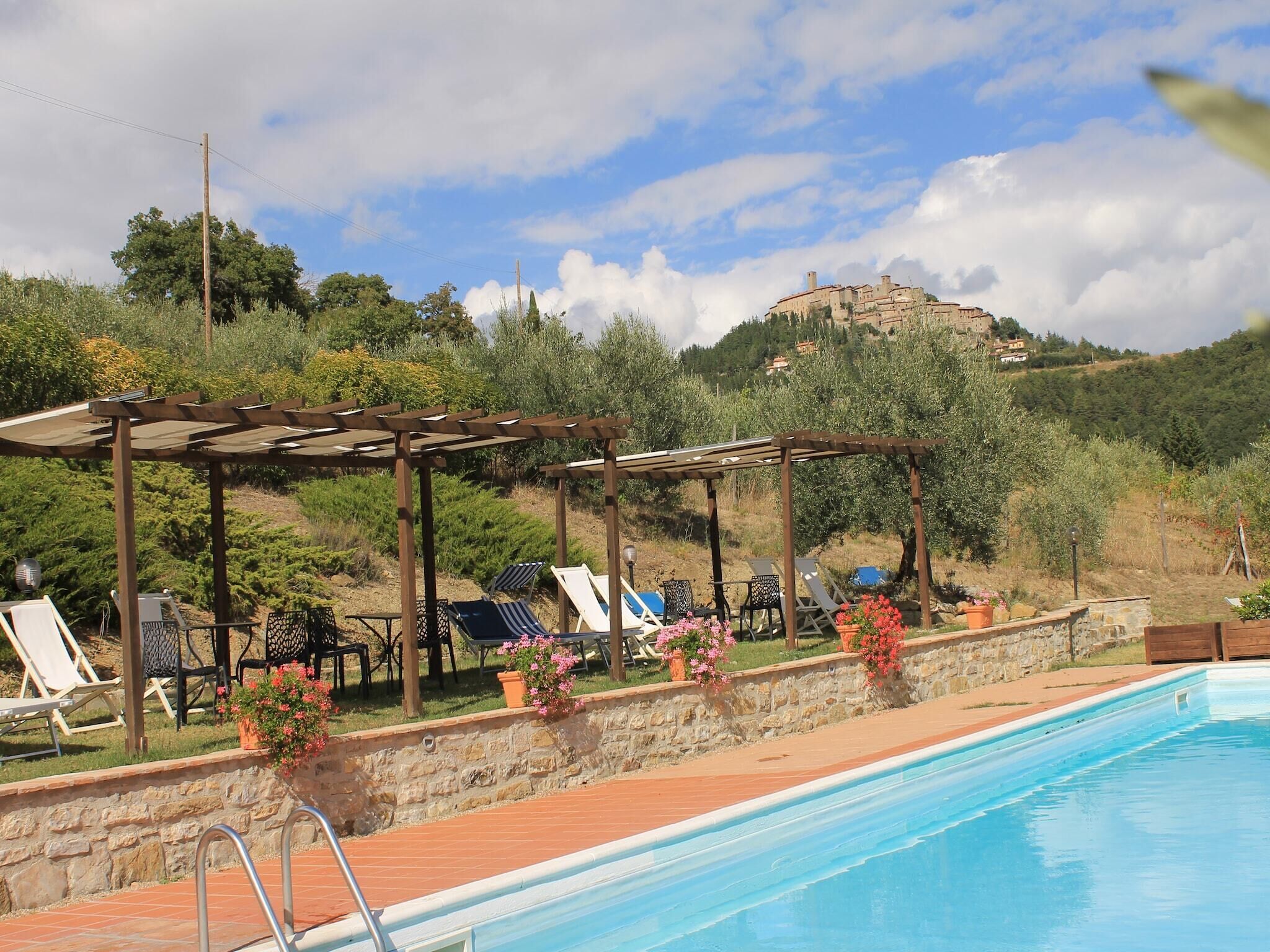 A swimming pool with lounge chairs and a pergola, surrounded by stone walls and potted plants.