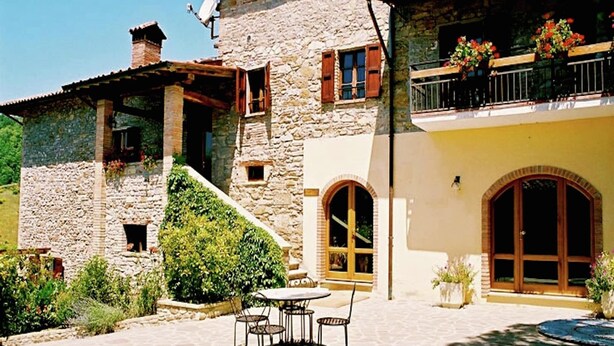 Un bâtiment en pierre doté d’un balcon, de sièges en plein air et d’un escalier menant à un niveau supérieur.