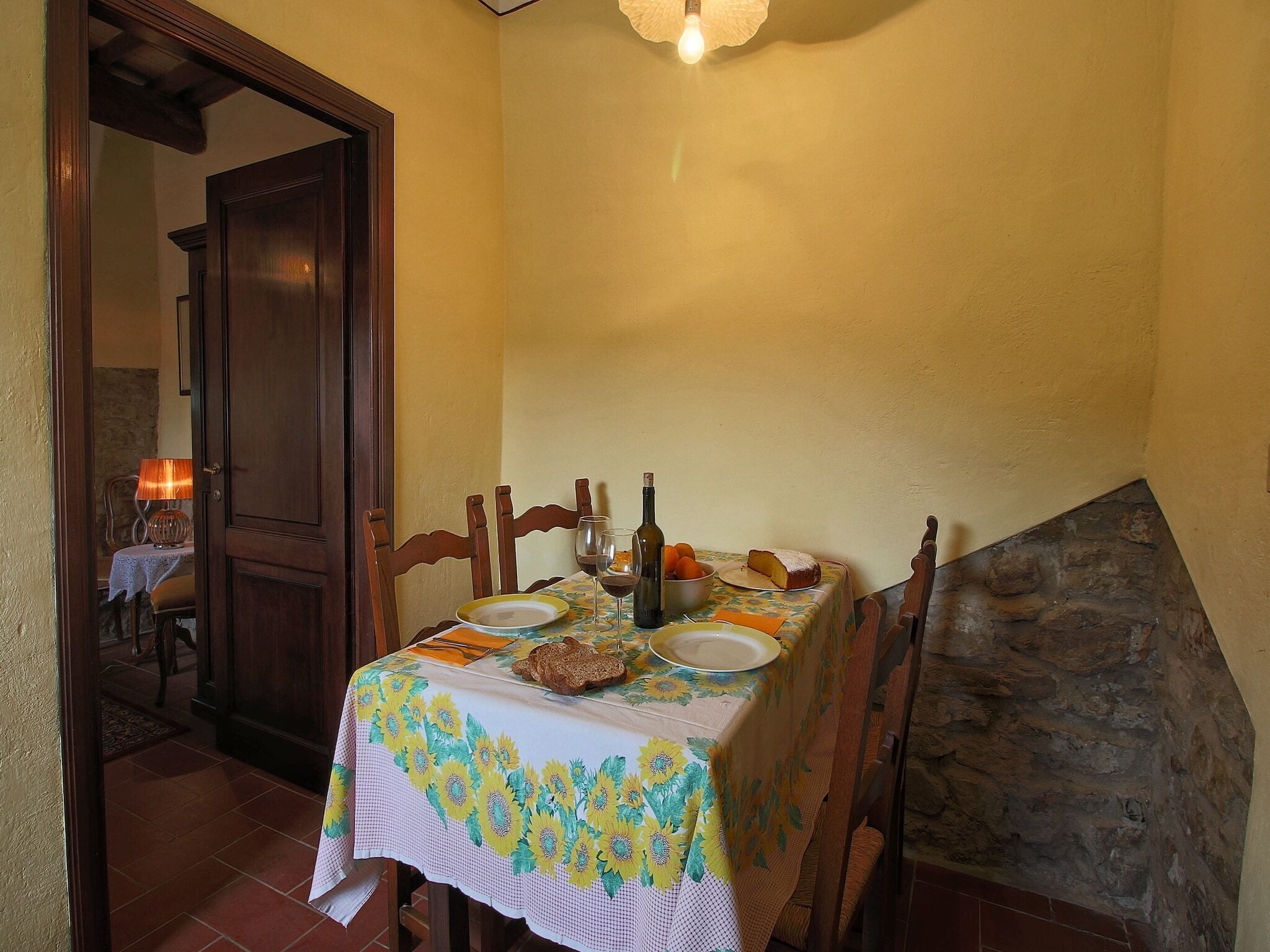 A dining area with a table set for two, a bottle of wine, a plate of food, and a bread roll.