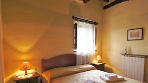 Ein Schlafzimmer mit einem Bett, zwei Nachttischen mit Lampen, einem Heizkörper und einem Fenster mit Vorhängen.