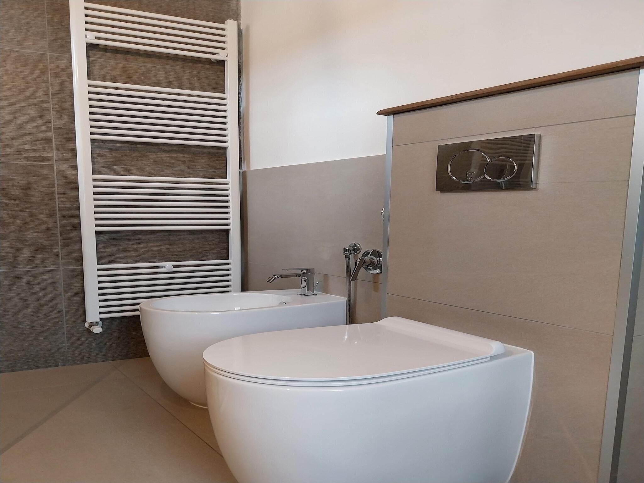 Un baño moderno con dos inodoros blancos, un lavamanos blanco y una ducha con grifo cromado.