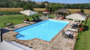 Ein rechteckiger Pool mit einer Steinterrasse, umgeben von Liegestühlen und Sonnenschirmen, vor ländlicher Kulisse.
