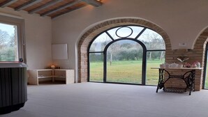 Ein geräumiger Raum mit einem großen Bogenfenster, einem Holztisch mit Küchenutensilien und einer Heizung.
