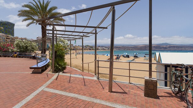 Une promenade en bord de mer agrémentée d’une pergola en métal, de bancs et d’un abri à vélos.