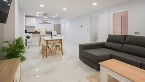 Un salon moderne avec un canapé gris, une table basse en bois et un coin repas comprenant une table et des chaises blanches.