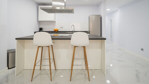 Une cuisine moderne dotée d’un îlot central, de deux tabourets de bar, d’une hotte en acier inoxydable et d’un réfrigérateur.