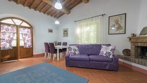 A cozy living room with a purple sofa, a dining table with chairs, a fireplace, and a large window with curtains. - Escape in Rosignano Hills (Rosignano Marittimo)