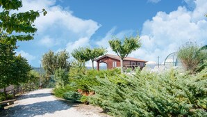 A red building with a covered patio area, surrounded by lush greenery and a gravel path. - Farmhouse in Apecchio with Panoramic Views (Apecchio)