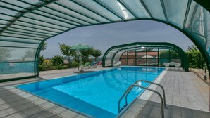 An indoor swimming pool with a glass ceiling, surrounded by lounge chairs and a small garden area. - Farmhouse in Apecchio with Panoramic Views (Apecchio)