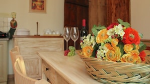 Een keuken met een houten tafel, een rieten mand met bloemen, wijnglazen en een fles wijn.