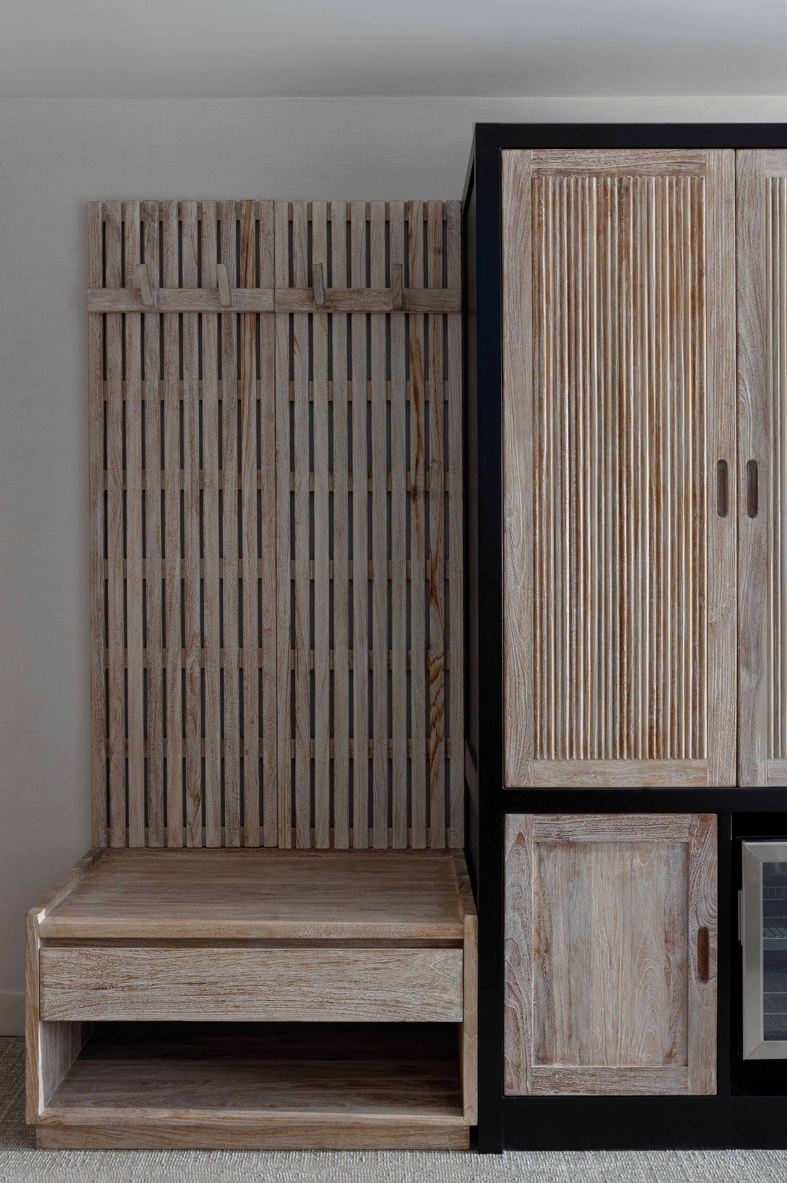 A wooden bench with a slatted backrest and a lower shelf, placed against a wall with a vertical wooden panel design.