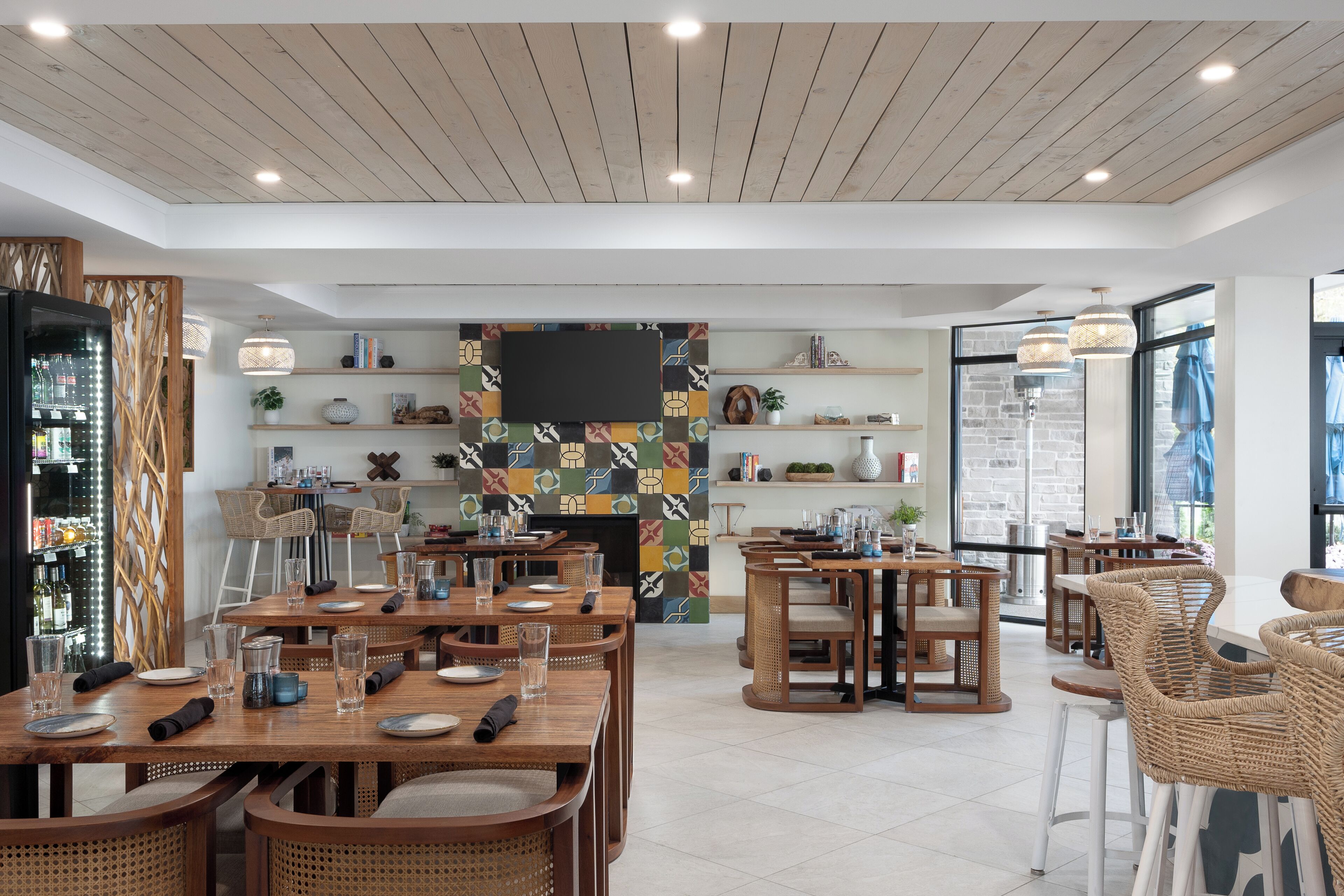 A modern restaurant with wooden tables and chairs, a fireplace, and shelves with books and decorative items.