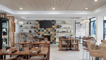 A modern restaurant with wooden tables and chairs, a fireplace, and shelves with books and decorative items.