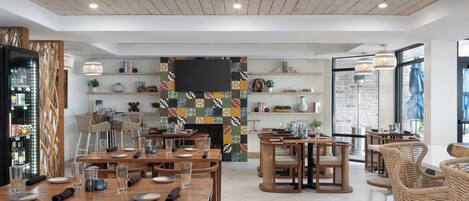 Um restaurante moderno com mesas e cadeiras de madeira, lareira e prateleiras com livros e objetos decorativos.