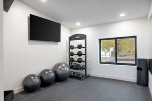 Un gimnasio moderno con una televisión instalada en la pared, un soporte para kettlebells y pelotas de ejercicio.